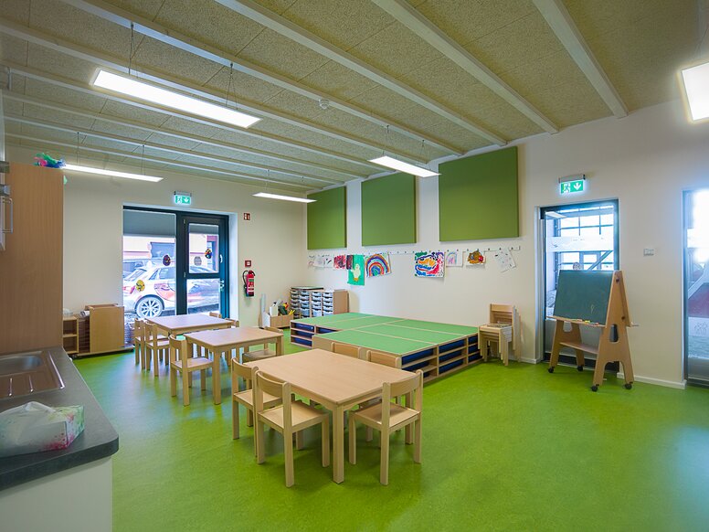 Gruppenraum der Kindertagesstätte „In der Kammgarnspinnerei“ Gruppenraum einer Kindertagesstätte mit grünem Boden und Tischen und Stühlen aus Holz